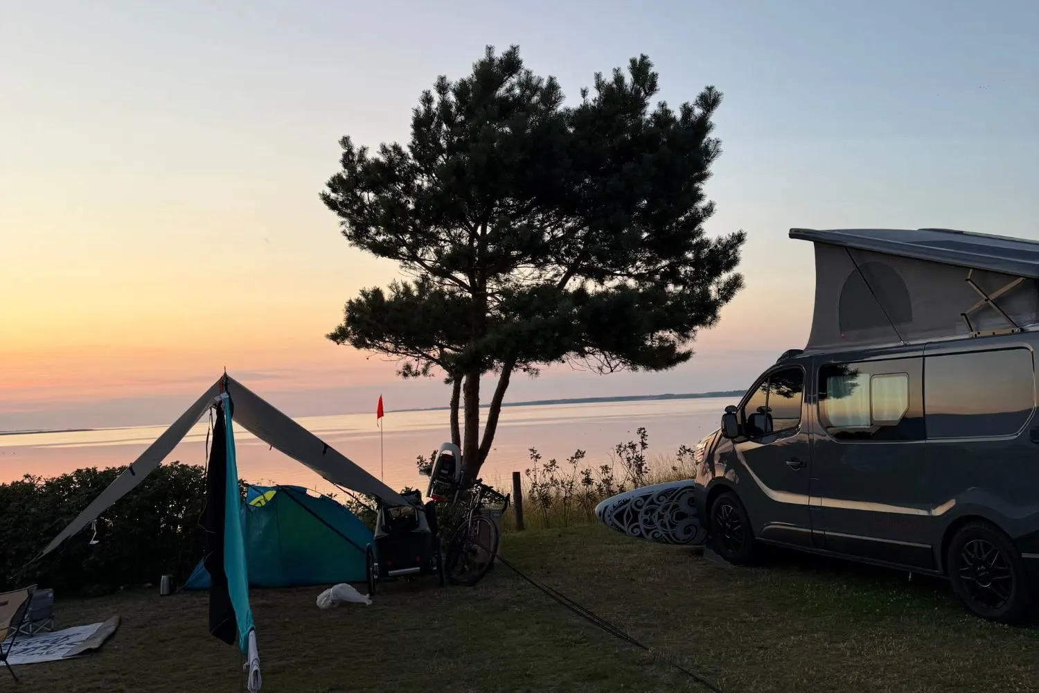 Campervan met hefdak en tent aan de fjord bij zonsondergang boven de Limfjord