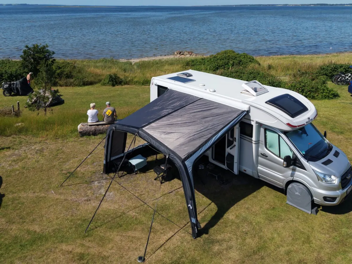 Motorhome with awning, and two guests on a bench overlooking the Limfjord