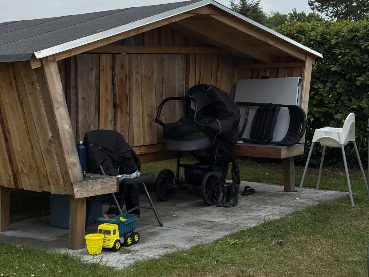 Shelter met overkapping en bankjes, in gebruik bij een gezin met kinderwagen