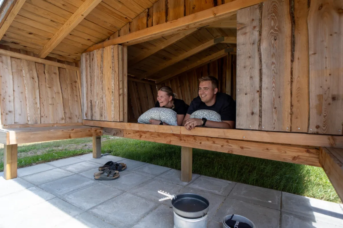 Twee gasten kijken uit de shelter met tegels en kookgerei ervoor