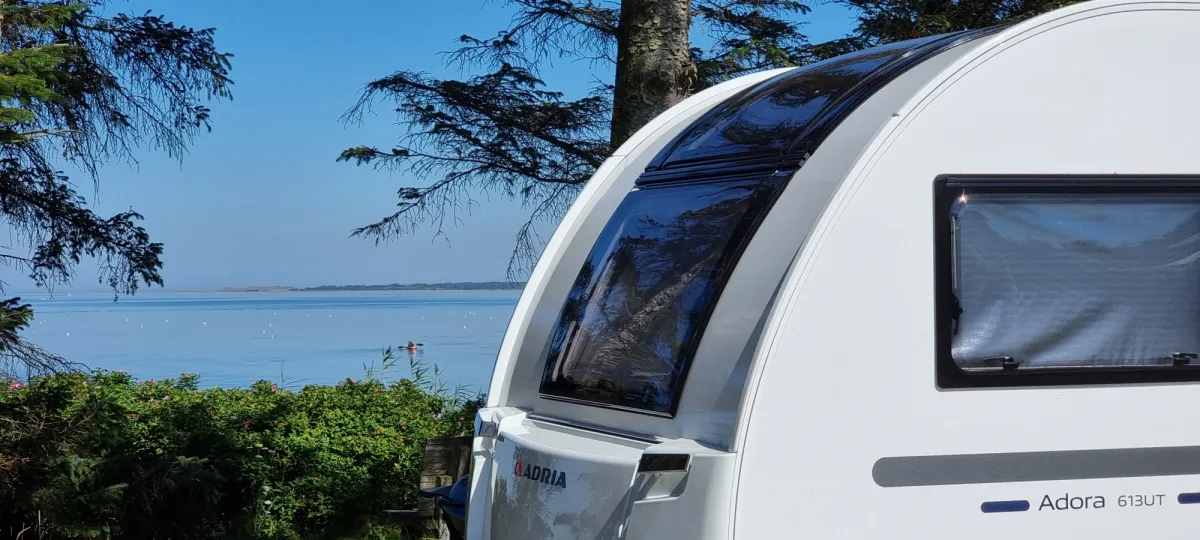 Caravan among the trees with a view of the fjord and a kayak on the water