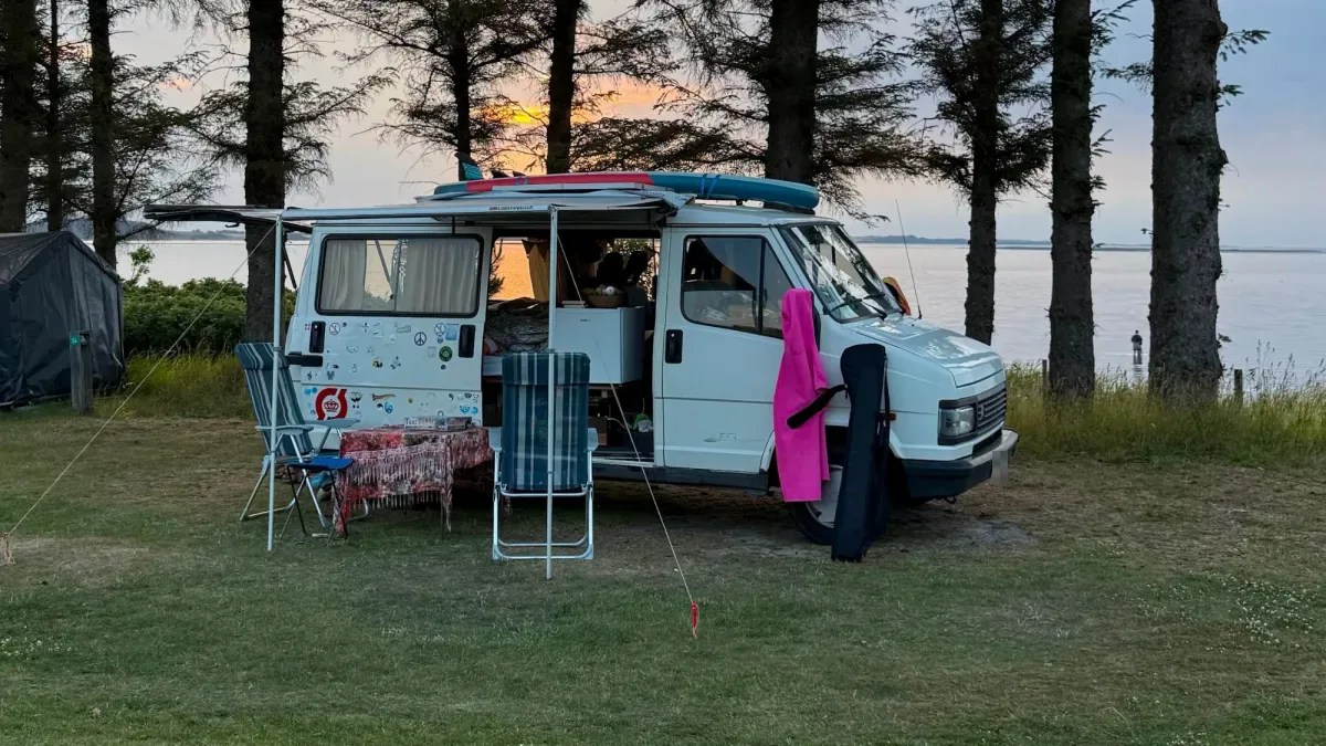 Campervan with awning, chairs and SUP board in the evening sun by the fjord