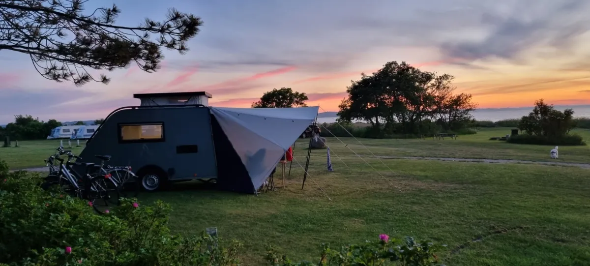 Small caravan with a sun canopy at sunset on a view pitch by the fjord