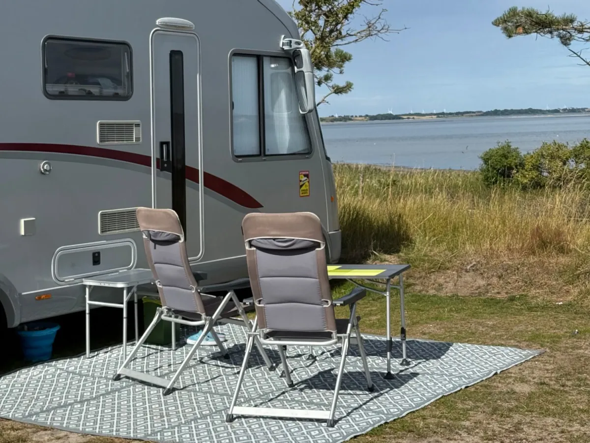 Motorhome with chairs and table on a view pitch under the pine trees with the Limfjord right in front
