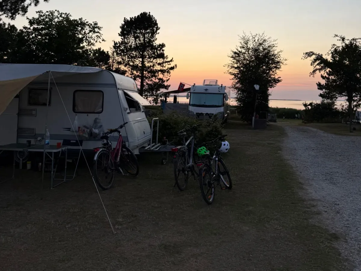 Caravan, fietsen en camper langs het grindpad bij zonsondergang met de Limfjord erachter