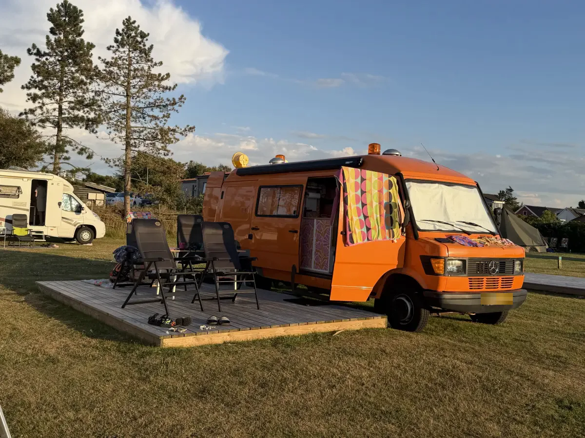 Orange motorhome on a view pitch with a wooden deck, chairs and table